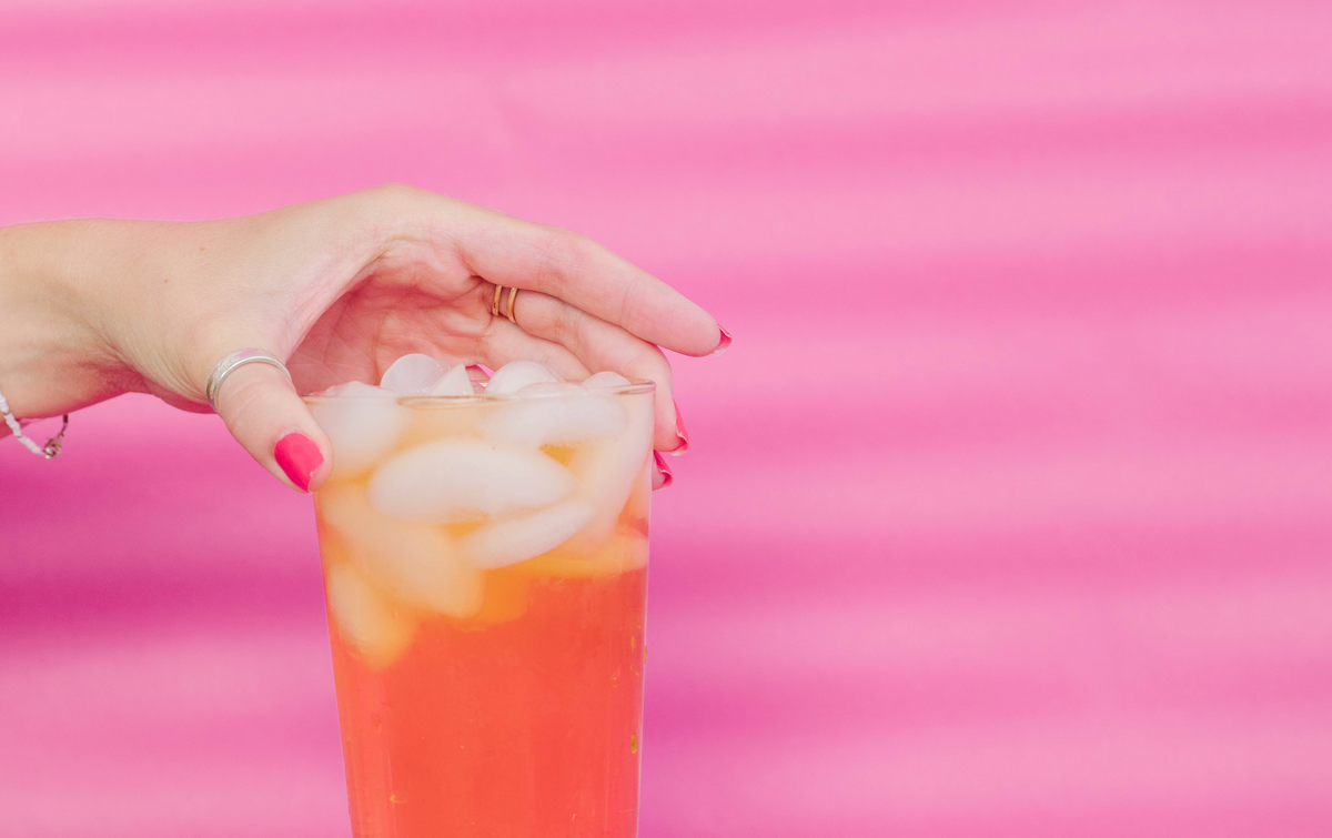 hand holding drink with pink backdrop